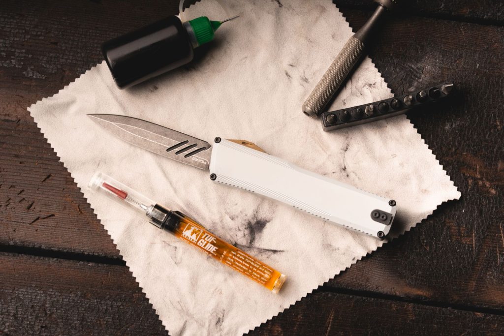 An Axial Shift III OTF automatic knife on a used microfiber cloth next to some OTF lube and tools.