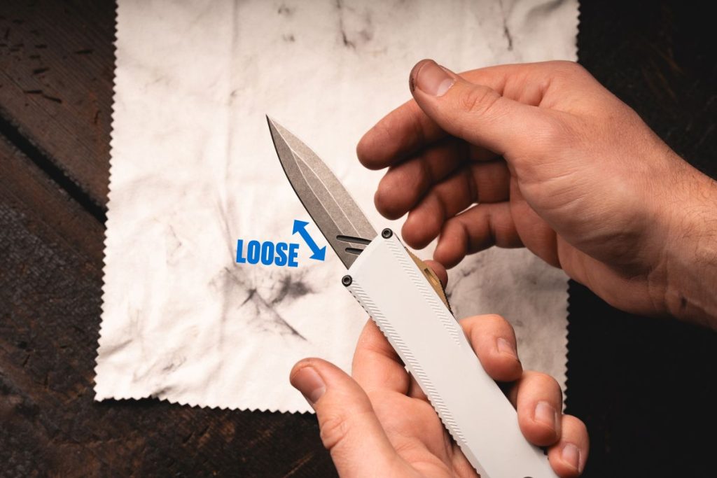 A man holding an OTF knife with a loose blade that's off track.