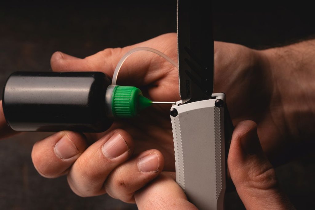 A man applying OTF lube to an OTF knife at the base of the blade.