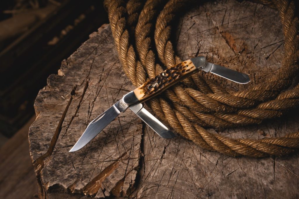 A large Case Stockman with orange peach seed jig bone handle scales on a stump with rope.