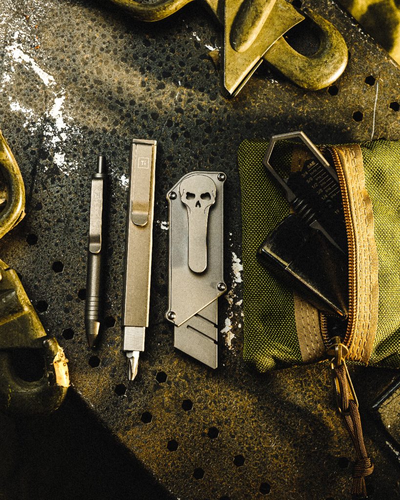 Titanium pens, tools, and box cutter utility tool in a flat lay format.