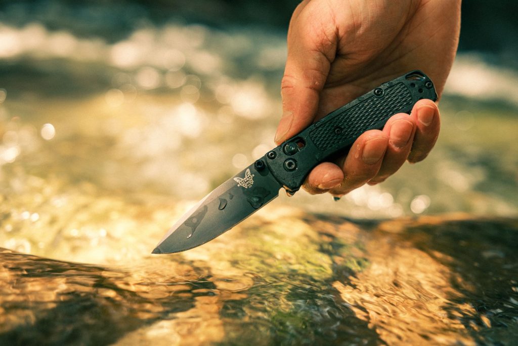 Black Benchmade Bugout covered in water droplets in hand, held over a stream.