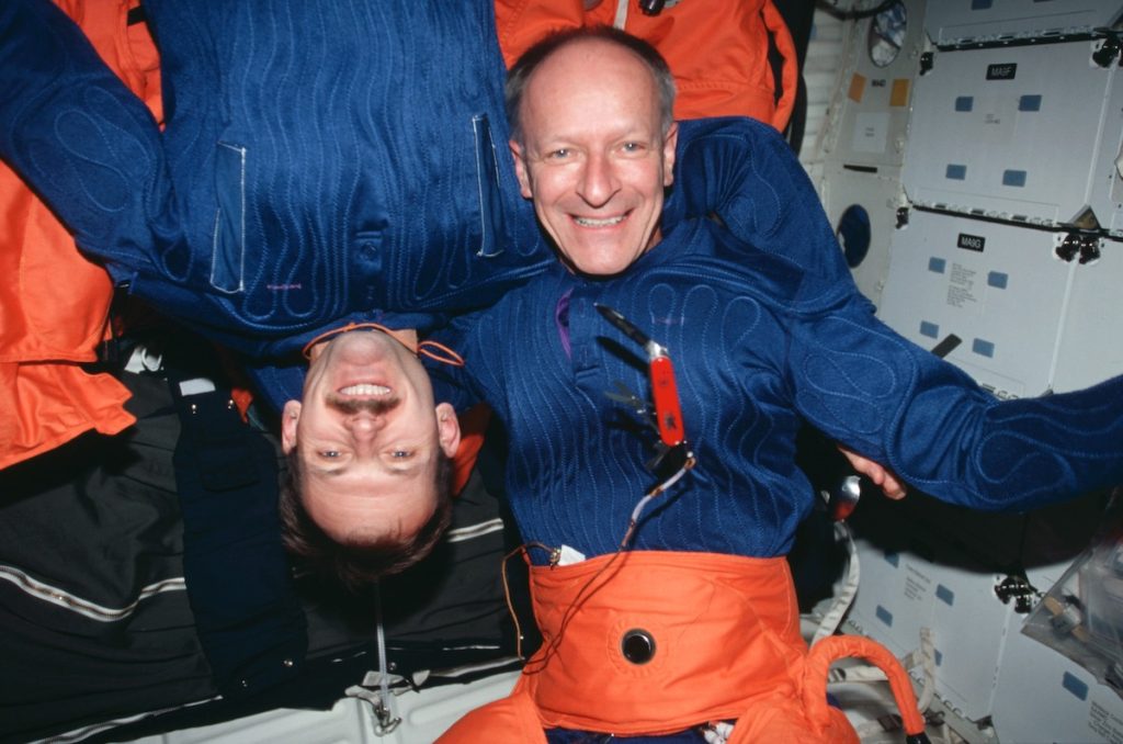 Two astronauts aboard the space shuttle Discovery, a Swiss Army Knife floats in front of them.