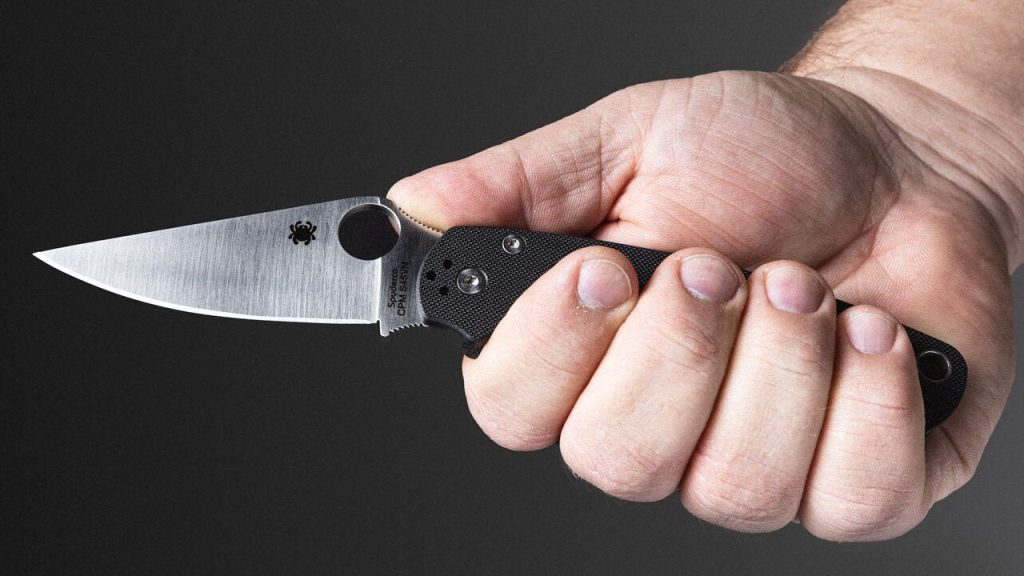A Spyderco Paramilitary 2 in a man's hand against a black background.