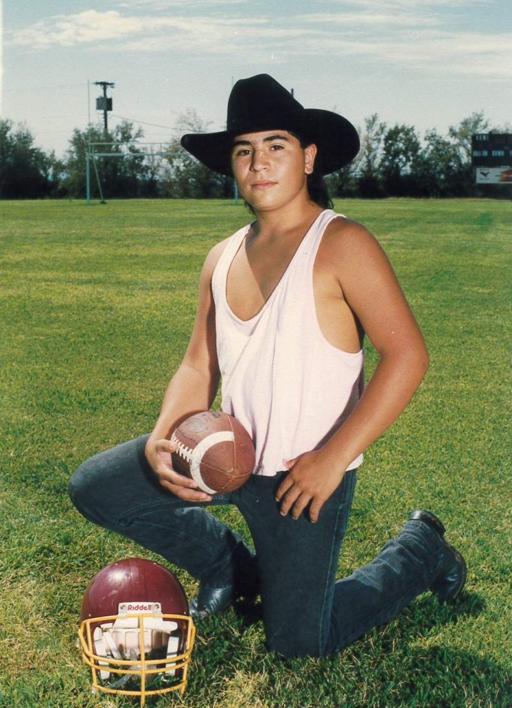 Teenage Ramon kneeling with a football, a football helmet in the grass beside him.