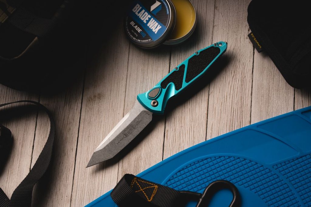 A blue Microtech Socom Elite on a table next to tactical gear.