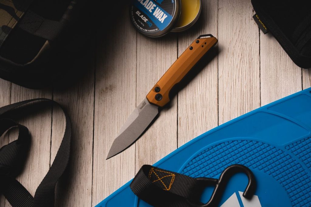 An orange Kershaw Launch Iridium automatic knife on a table next to some gear.