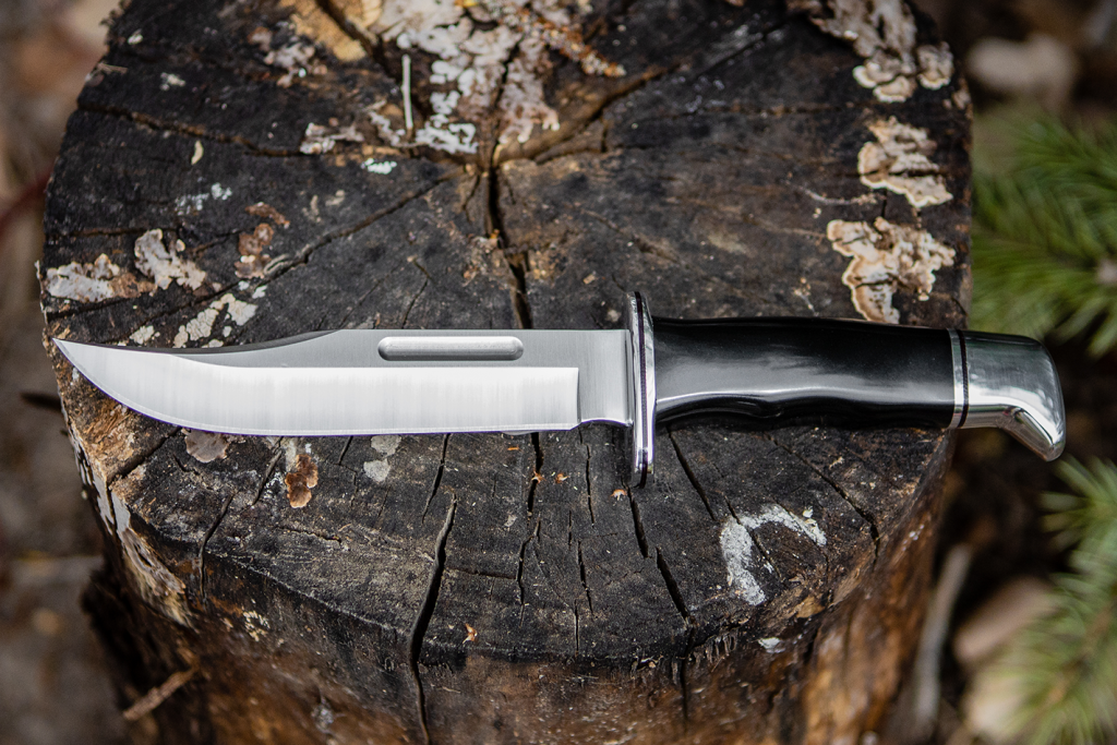 A buck Bowie-style knife on a stump.