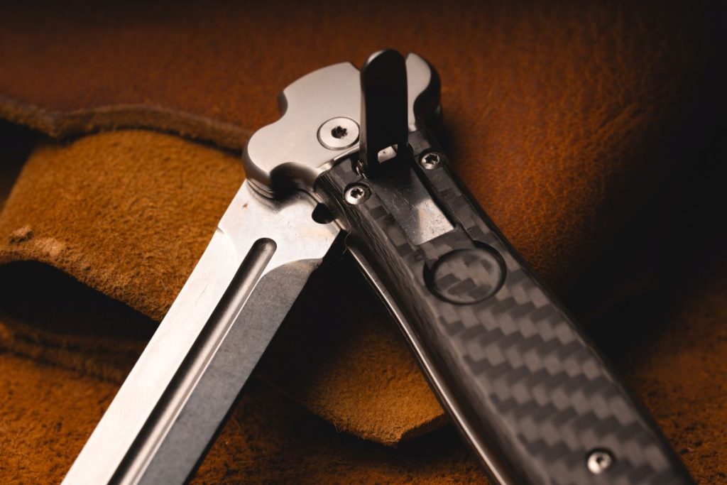 A half-open AGA Compolin Zero+ lever lcok automatic knife. It's half-open, lever up, on a leather mat.