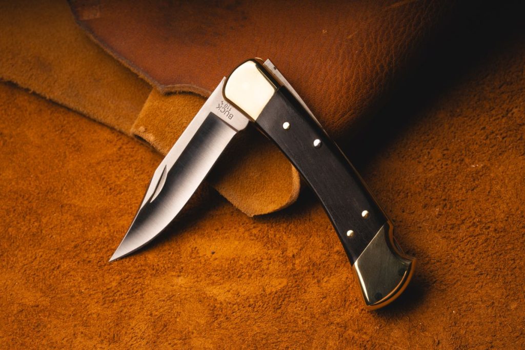 A Buck 110 lockback knife partially open against a leather background.