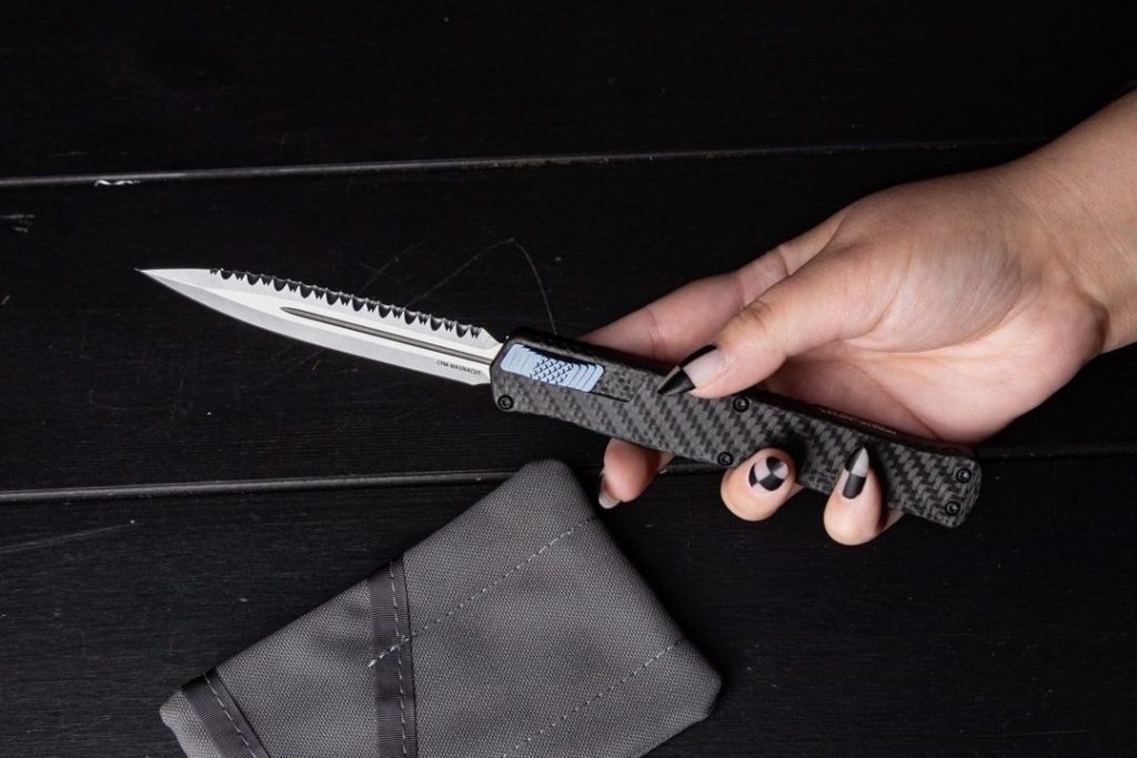 A Heretic Cleric II with a carbon fiber handle in a woman's hand. She has checkerboard-pattern nails.