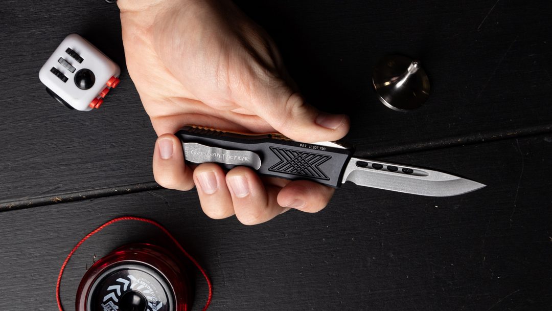 A Guardian Tactical GTX-025 automatic OTF knife in a man's hand. He's using the thumb slide to deploy the blade.