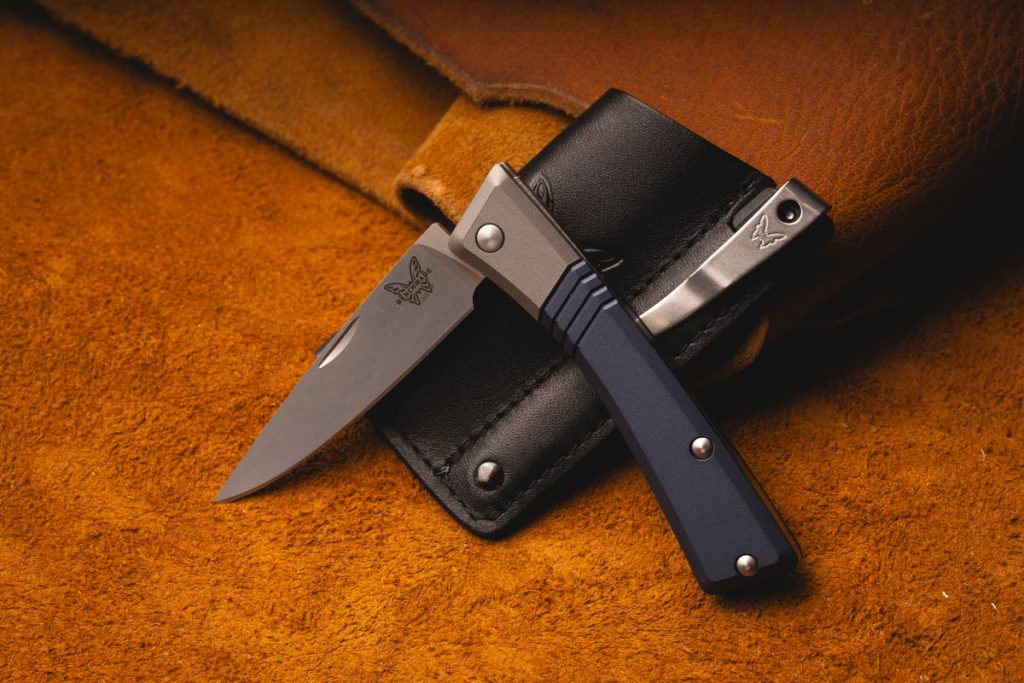 A Benchmade Successor with a nail nick opener. It's resting on its sheath against a brown leather background. 