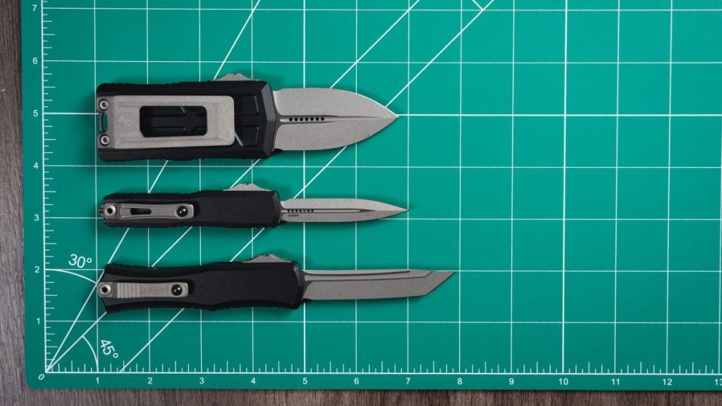 All mini Microtech OTF knives lined up on a green mat